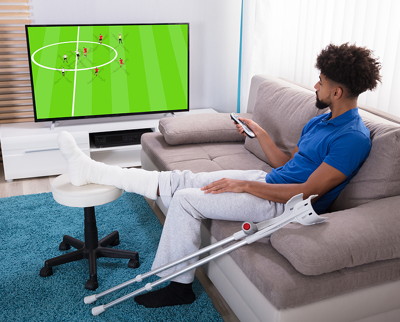 player with broken leg and crutches watching football on tv